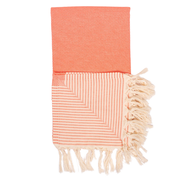 A cotton towel in an orange color with a subtle striped pattern and white fringe.